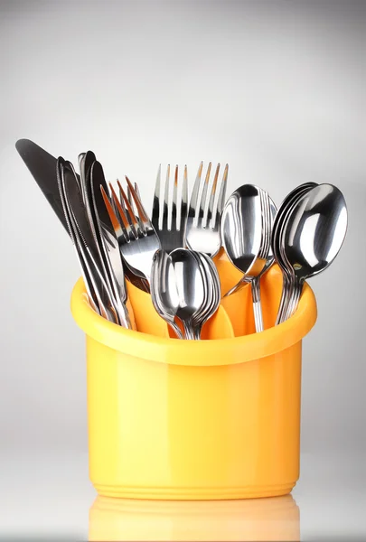 Posate da cucina, coltelli, forchette e cucchiai in stativo giallo su fondo grigio — Foto Stock