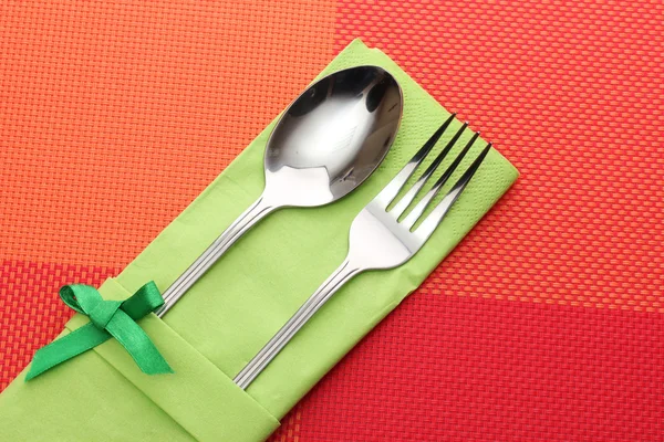 Tenedor y cuchara en un paño verde con un lazo sobre un mantel rojo —  Fotos de Stock