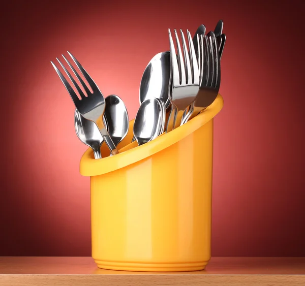 Κουζίνα μαχαιροπήρουνα, μαχαίρια, πιρούνια και κουτάλια με κίτρινο χρώμα σταθεί σε κόκκινο φόντο — Φωτογραφία Αρχείου