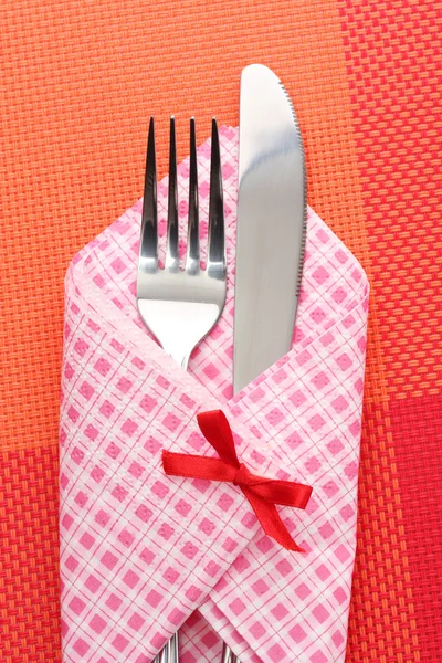 Fork and knife in a plaid cloth with a bow on a red tablecloth — Stock Photo, Image