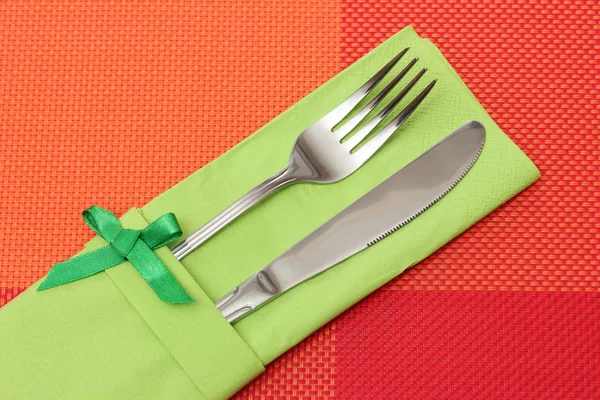 Garfo e faca em um pano verde com um arco em uma toalha de mesa vermelha — Fotografia de Stock