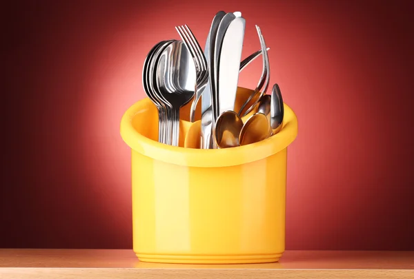 Cubertería de cocina, cuchillos, tenedores y cucharas en soporte amarillo sobre fondo rojo — Foto de Stock