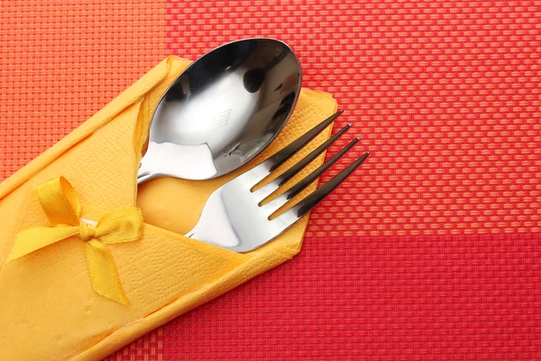 Fork and spoon in a yellow cloth with a bow on a red tablecloth — Stock Photo, Image