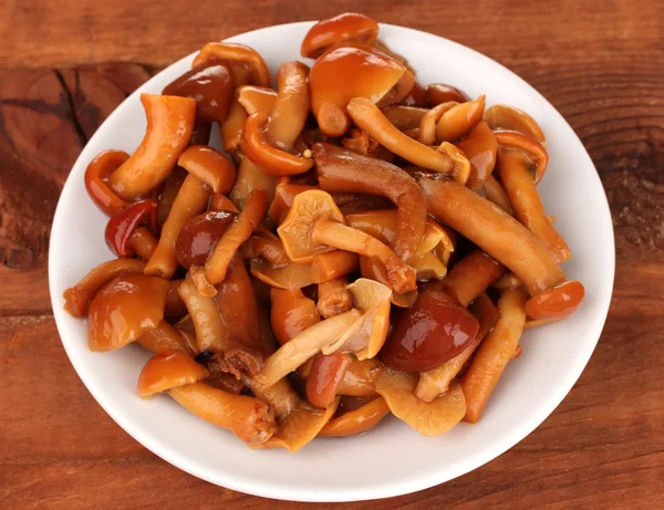 Маринованные грибы в блюдце на деревянном столе — стоковое фото