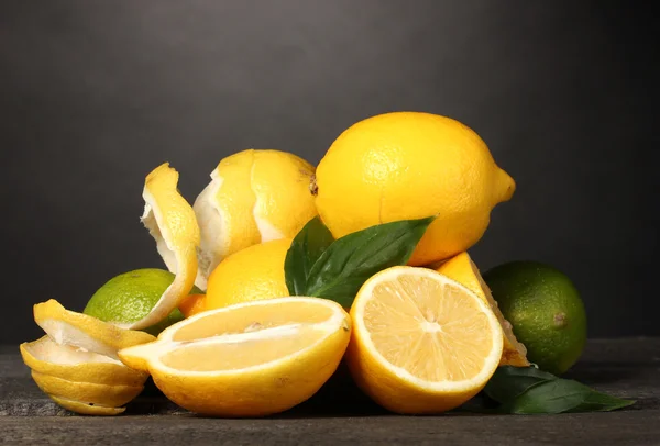 Dojrzałe cytryny i limonki z liści na drewnianym stole na szarym tle — Zdjęcie stockowe