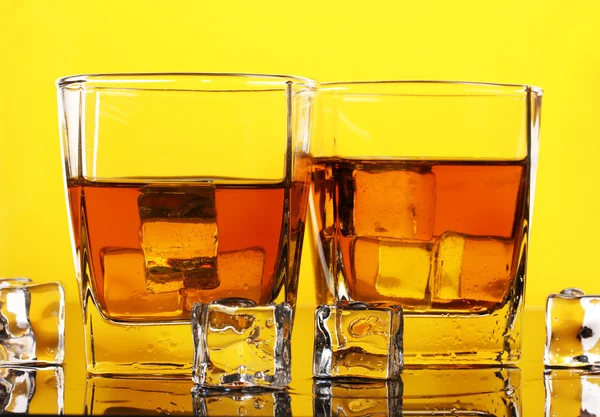 Twee glazen van scotch whisky en ijs op gele achtergrond — Stockfoto
