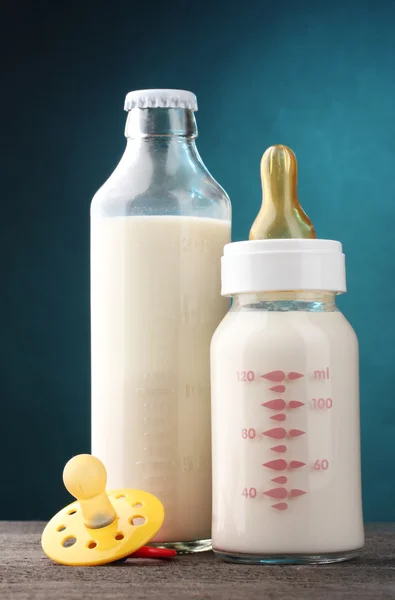 Flessen van melk en fopspeen op houten tafel op blauwe achtergrond — Stockfoto