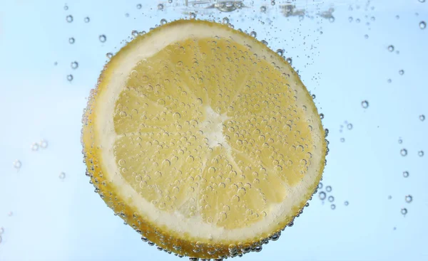 Tranche de citron dans l'eau bleue avec des bulles — Photo