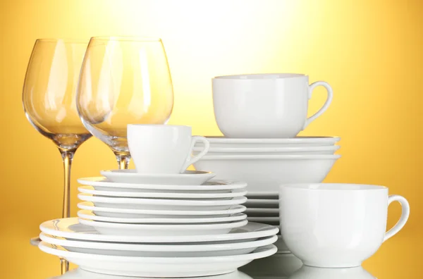Ciotole vuote, piatti, tazze e bicchieri su sfondo giallo — Foto Stock
