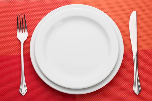 포크와 나이프는 빨간색 식탁보에 흰색 빈 접시 — 스톡 사진