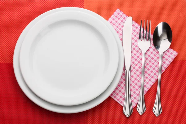 Λευκό άδειο πιάτο με πιρούνι, κουτάλι και μαχαίρι για ένα κόκκινο τραπεζομάντιλο — Φωτογραφία Αρχείου