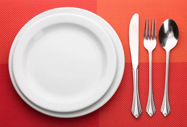 Assiette vide blanche avec fourchette, cuillère et couteau sur une nappe rouge — Photo