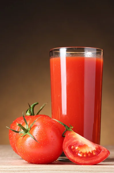 Jugo de tomate en vaso y tomate sobre mesa de madera sobre fondo marrón —  Fotos de Stock