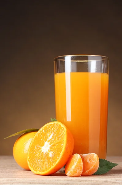 Mandarini e succo di vetro su tavolo di legno su sfondo marrone — Foto Stock