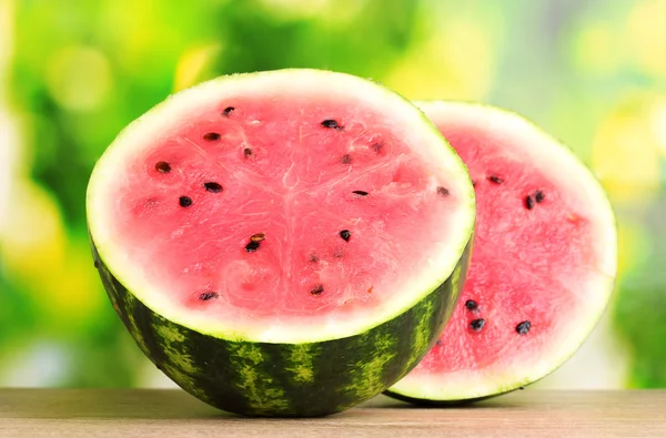 Rijpe zoete watermeloen op houten tafel op groene achtergrond — Stockfoto