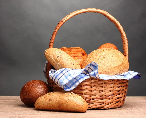 Delicious bread in basket on wooden table on gray background — Stock Photo, Image