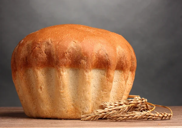 Вкусный круглый хлеб и уши на деревянном столе на сером фоне — стоковое фото