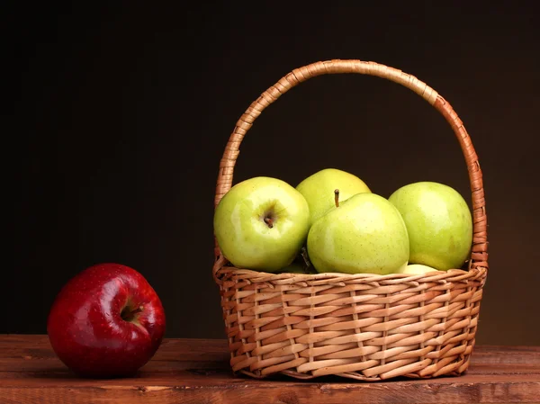 Juicy green apples in basket and red apple on wooden table on brown backgro — Stock Photo, Image