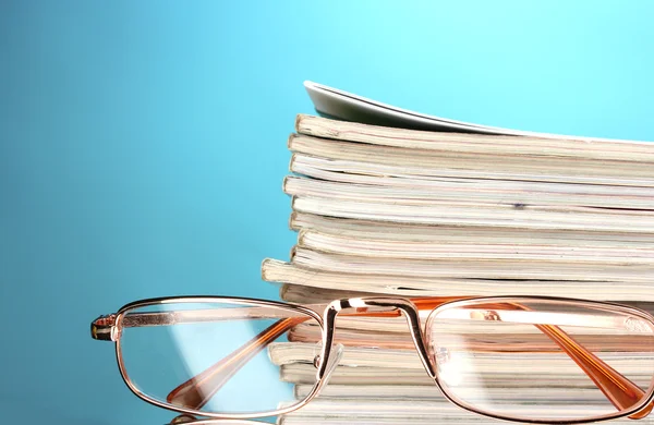 Stapel von Zeitschriften und Brillen auf blauem Hintergrund — Stockfoto