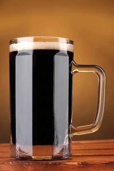 stock image Dark beer in a mug on wooden table on brown background