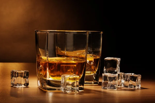 Stock image Two glasses of scotch whiskey and ice on wooden table on brown background