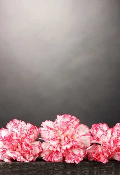 Schöne Nelken auf Holztisch auf grauem Hintergrund — Stockfoto