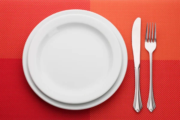 Белая пустая тарелка с вилкой и ножом на красной скатерти — стоковое фото