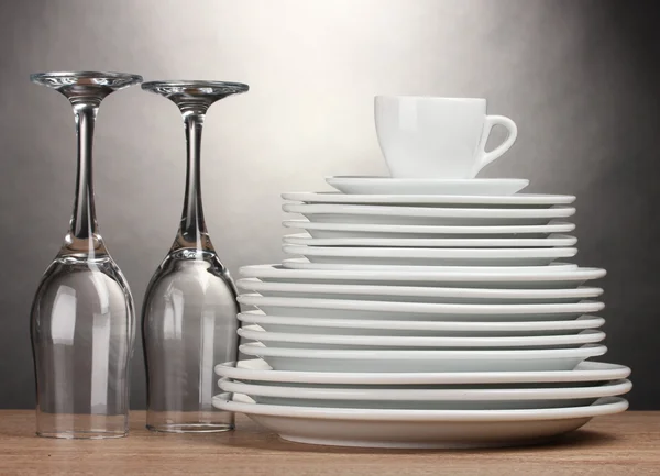 Piatti puliti, bicchieri e tazza su tavolo in legno su sfondo grigio — Foto Stock