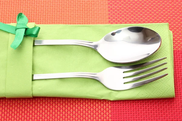 Fork and spoon in a green cloth with a bow on a red tablecloth — Stock Photo, Image