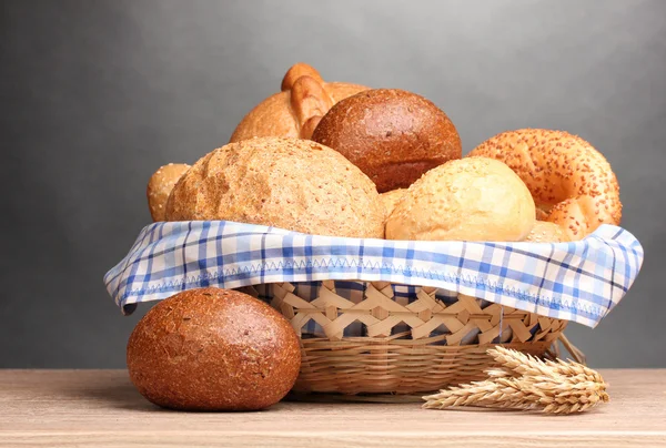 Pâine delicioasă în coș și urechi pe masă de lemn pe fundal gri — Fotografie, imagine de stoc
