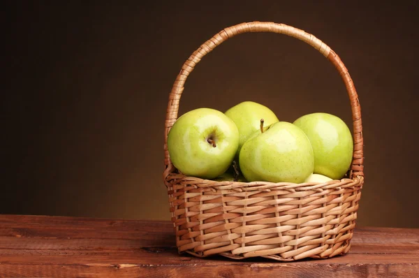Juicy green apples in basket on wooden table on brown background — Stock Photo, Image