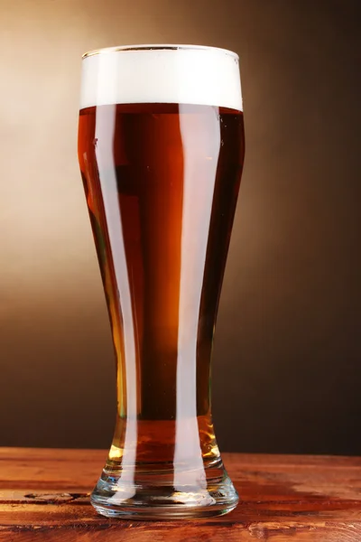 Beer in glass on wooden table on brown background — Stock Photo, Image