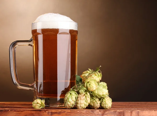 Bier mok en groen hop op houten tafel op bruine achtergrond — Stockfoto