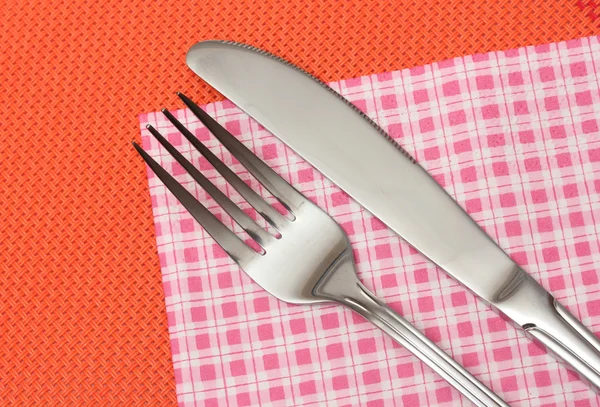 Forchetta e coltello in un panno a quadri su una tovaglia rossa — Foto Stock