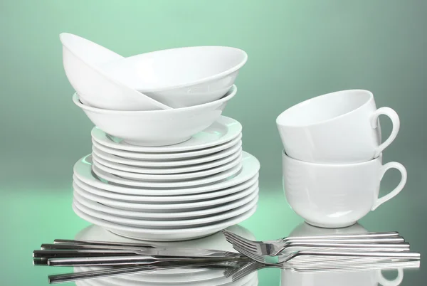Clean plates, cups and cutlery on green background — Stock Photo, Image