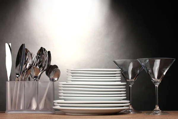 Clean plates, glasses and cutlery on wooden table on grey background