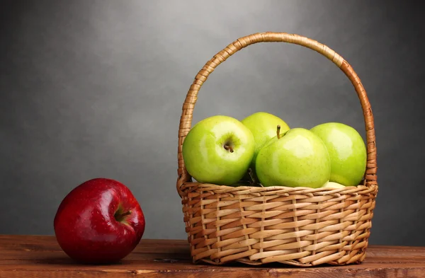 Manzanas verdes jugosas en cesta y manzana roja sobre mesa de madera sobre fondo gris —  Fotos de Stock