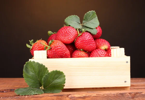 Aardbeien met bladeren in houten doos op tafel op bruine achtergrond — Stockfoto
