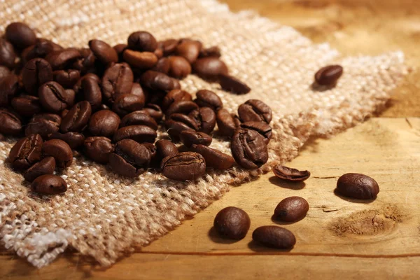 Granos de café en saqueo sobre mesa de madera — Foto de Stock