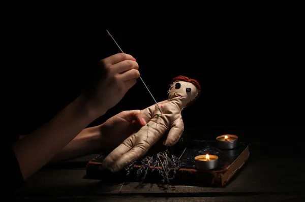 Muñeca vudú perforada por una aguja en una mesa de madera a la luz de las velas —  Fotos de Stock
