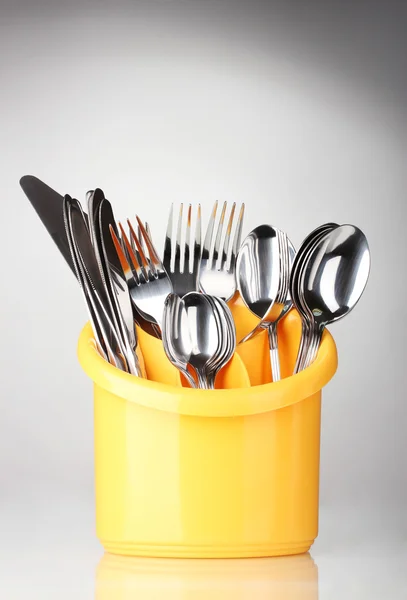 Кухонные столовые приборы, ножи, вилки и ложки в желтом стоят на серой спинке — стоковое фото