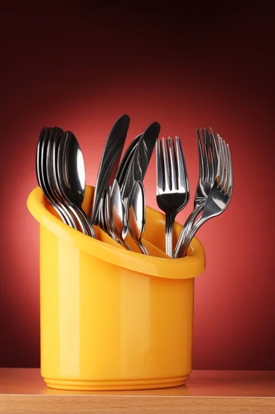 Keuken bestek, messen, vorken en lepels in geel staan op rode achtergrond — Stockfoto