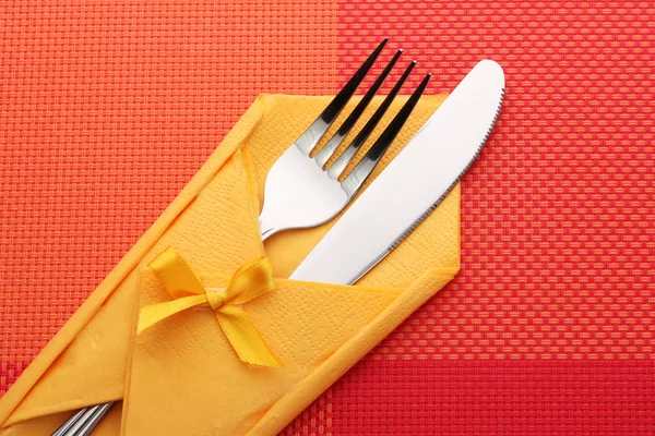 Garfo e faca em um pano amarelo com um arco em uma toalha de mesa vermelha — Fotografia de Stock