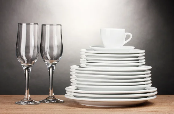Чистые тарелки, стаканы и чашки на деревянном столе на сером фоне — стоковое фото