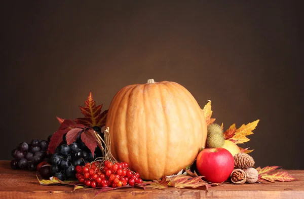 stock image Pumpkin, apples,berries and leaves on wooden table on brown background