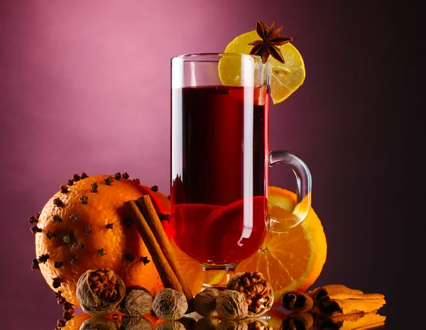 Vinho quente no copo, tempero e laranja no fundo roxo — Fotografia de Stock