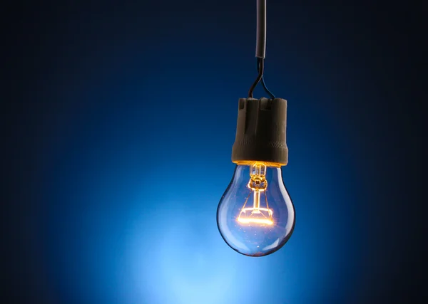Una lampadina accesa su sfondo blu — Foto Stock
