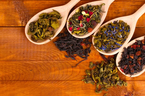 木製の背景にスプーンでの乾緑茶と黒茶の種類 — ストック写真