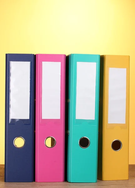 Яркие офисные папки на деревянном столе на желтом фоне — стоковое фото