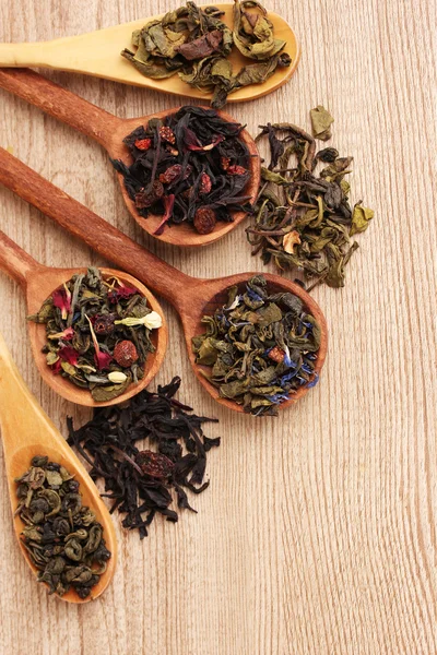 Verschiedene Arten von grünem und schwarzem Tee in Löffeln auf Holztisch — Stockfoto